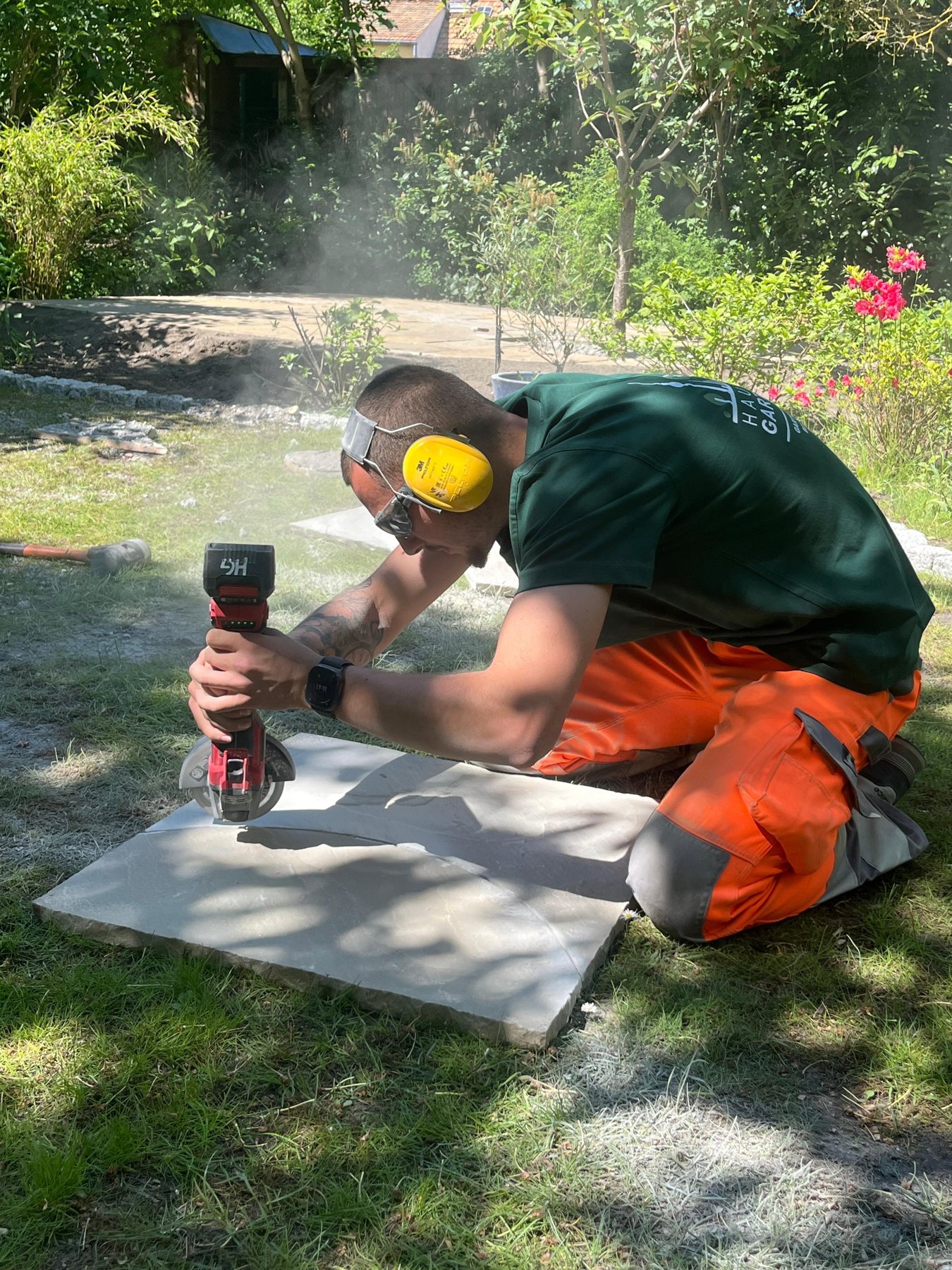 Mitarbeiter von Hauptstadt Gartenpflege beim Zuschnitt einer Terrassenplatte mit Gehörschutz und Schutzbrille